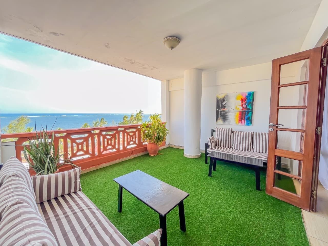A balcony with artificial grass, a sofa, a table, and a bench.
