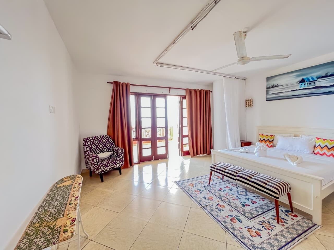 Hotelkamer met een bed, een stoel, een bank, een groot raam met gordijnen en een plafondventilator.