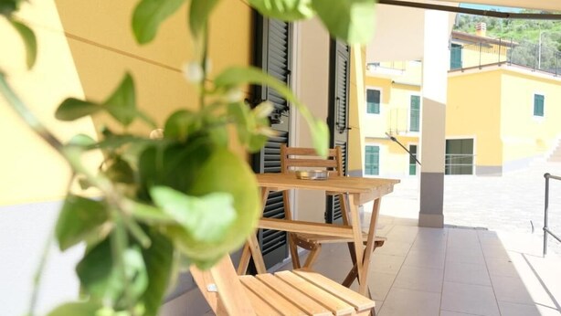 Et træbord og stole på en balkon med en gul bygning i baggrunden.