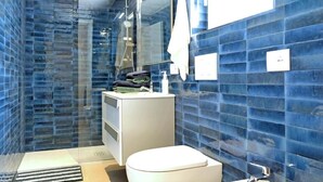 Et moderne badeværelse med blå klinkevægge, et glasbadeværelseskabine, en hvid vask og et toilet.