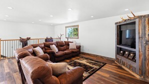 A spacious living room with a large brown leather sectional sofa, a wooden entertainment center, and a wooden floor. - Large house with lots of space. Just minutes away from national forest. (Thayne)