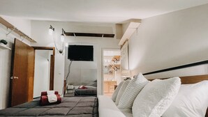 A modern bedroom with a large bed, a TV mounted on the wall, and a bathroom visible through an open door.