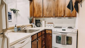 A kitchen with wooden cabinets, a white countertop, a coffee maker, a stove, and a dishwasher.