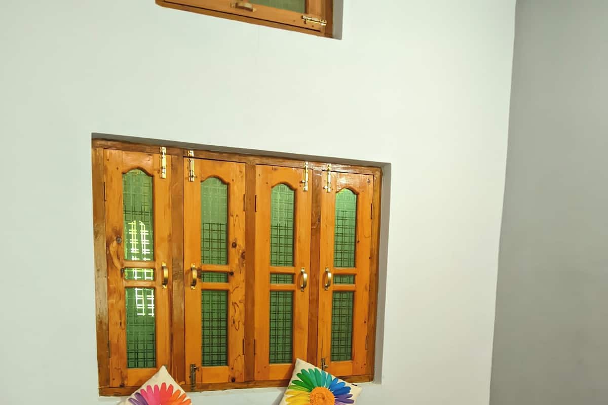 A room with a wooden bed, two colorful pillows, and a wooden door with glass panels.