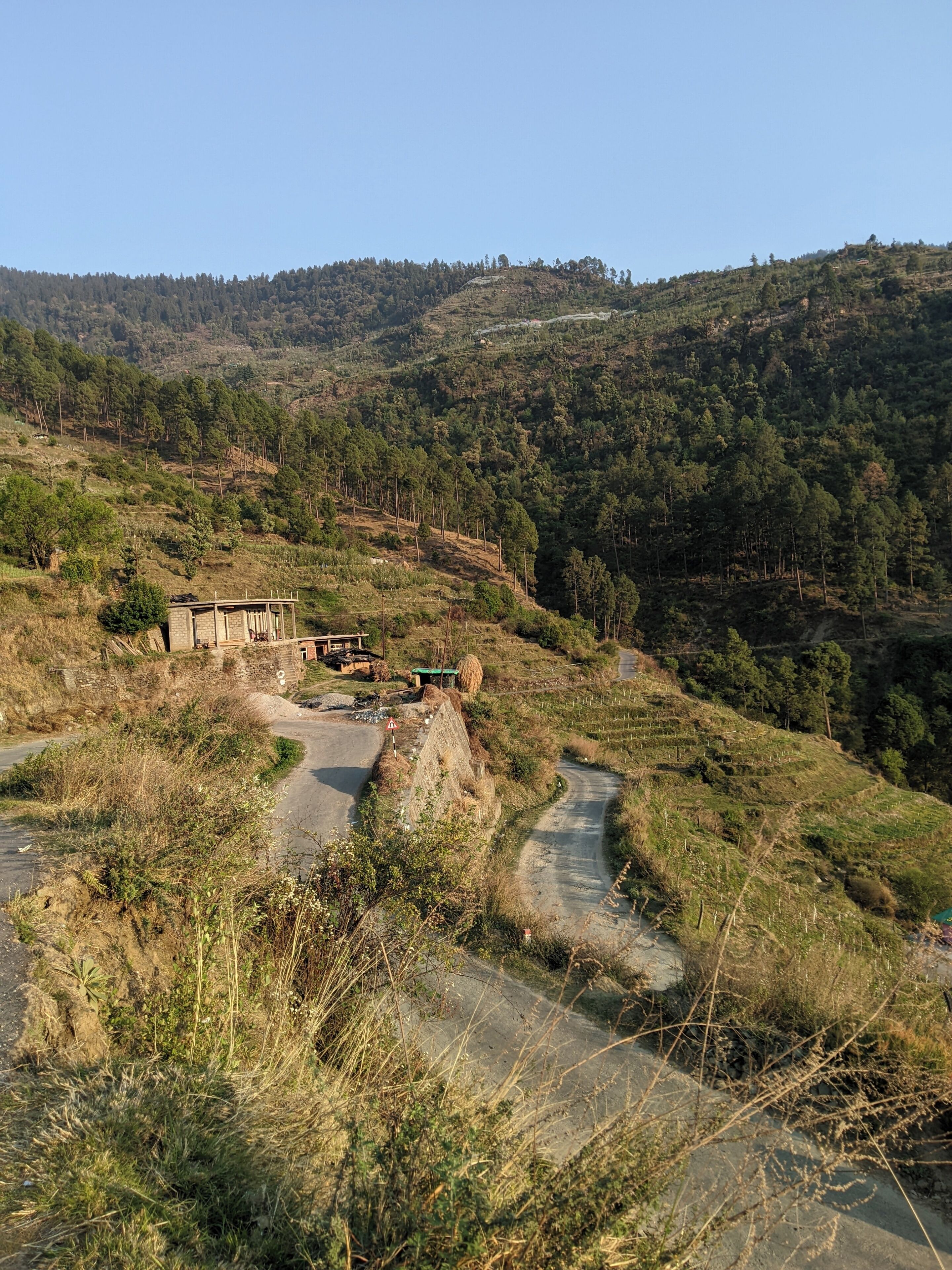 A rural road winding through a hilly landscape with a small building and a bridge.