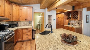 A kitchen with wooden cabinets, granite countertops, a stainless steel stove, and a wine rack. - Summit's Trident, Spa, Game Room, Snow Summit (Big Bear Lake)