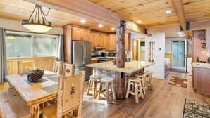 A wooden interior with a central island, wooden chairs, a dining table, and a kitchen area with appliances. - Summit's Trident, Spa, Game Room, Snow Summit (Big Bear Lake)