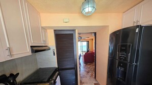 A kitchen with a black refrigerator, a stove, and a microwave. There is a door leading to a living area with a red couch and a view of the outdoors. - Ocean view condo with balcony hotel zone (Cancún)
