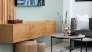A modern living room with a wooden cabinet, two round stools, a small round table, and a plant in a glass vase.