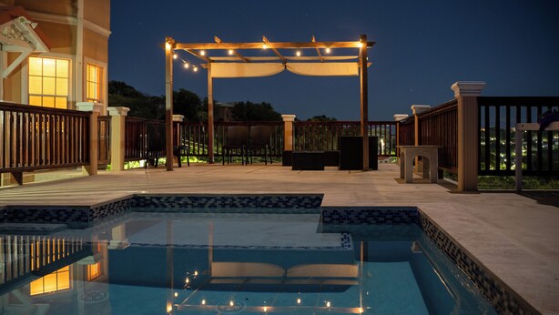 A pool area with a pergola and seating, surrounded by a wooden fence and a tiled deck.