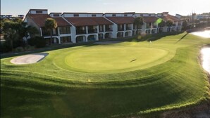 Golfkenttä, jossa on vesieste, hiekkabunkkeri ja taustalla punakattoinen rakennus.