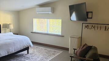 A bedroom with a bed, a chair, a TV, an air conditioner, and a window with blinds.