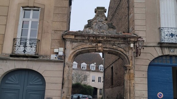 An arched entrance with a stone facade, a blue door, and a no parking sign.