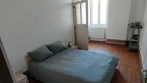 A bedroom with a bed, a nightstand, a radiator, and a window.