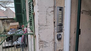 A building exterior with a metal gate, a wall-mounted intercom, and a utility box.