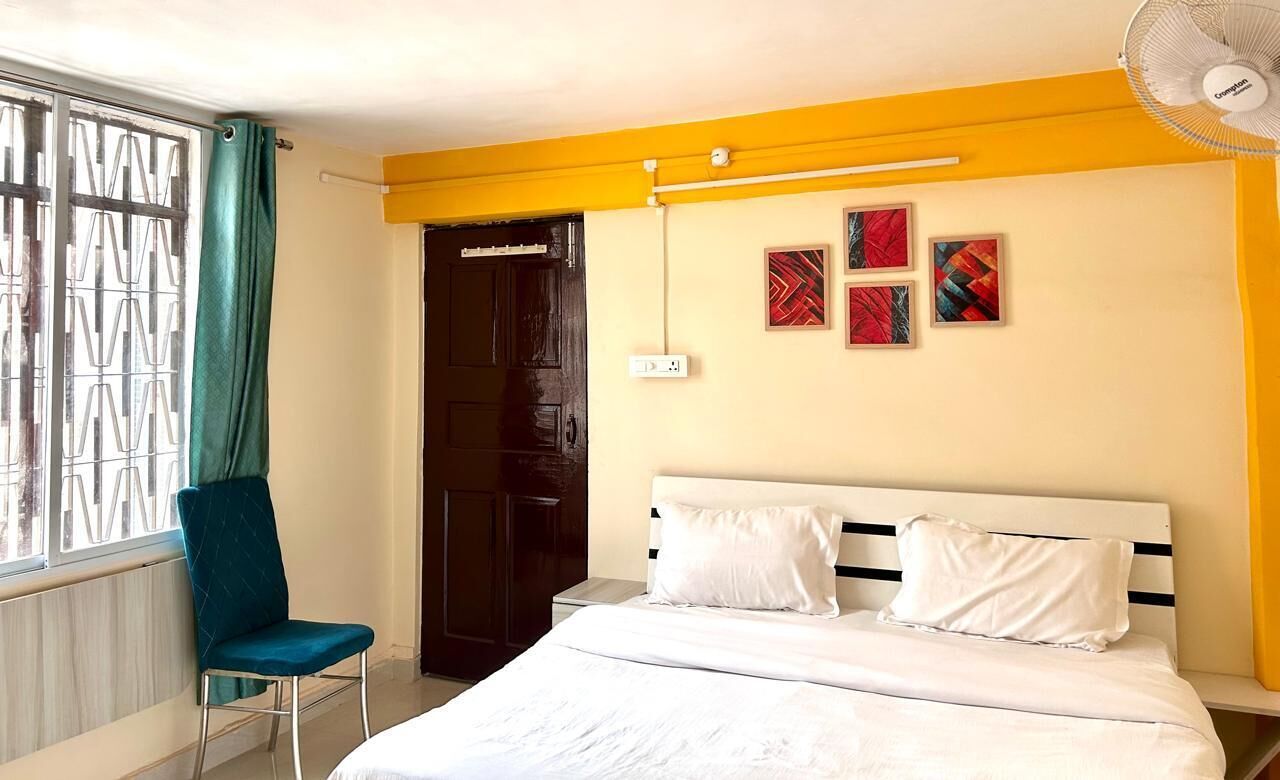 Een slaapkamer met een bed, een stoel, een raam met gordijnen en een deur.