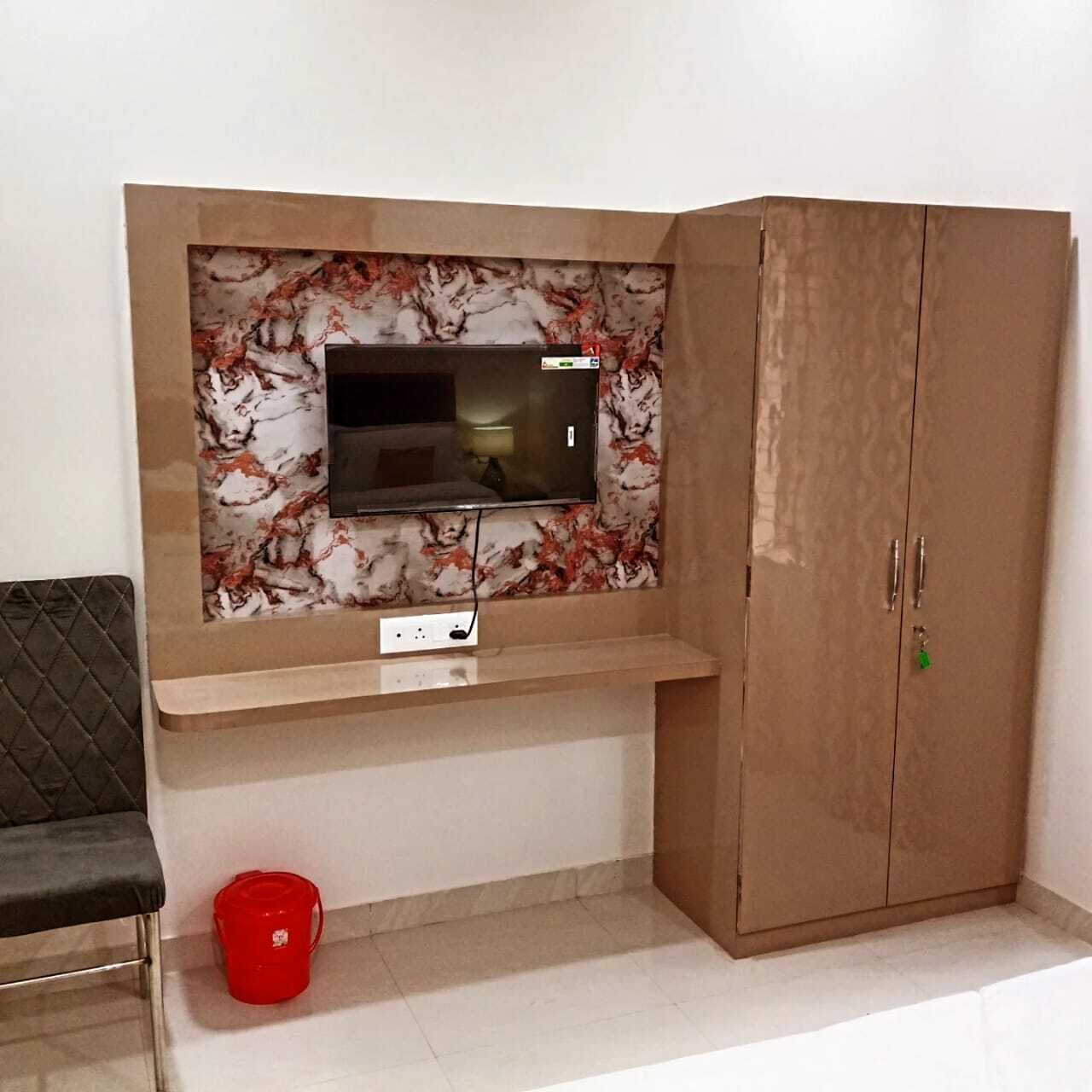 Een kamer met een aan de muur bevestigde televisie, een houten garderobe, een rode emmer en een zwarte stoel.