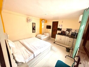 A hotel room with two beds, a small kitchenette, a mirror, and a window.