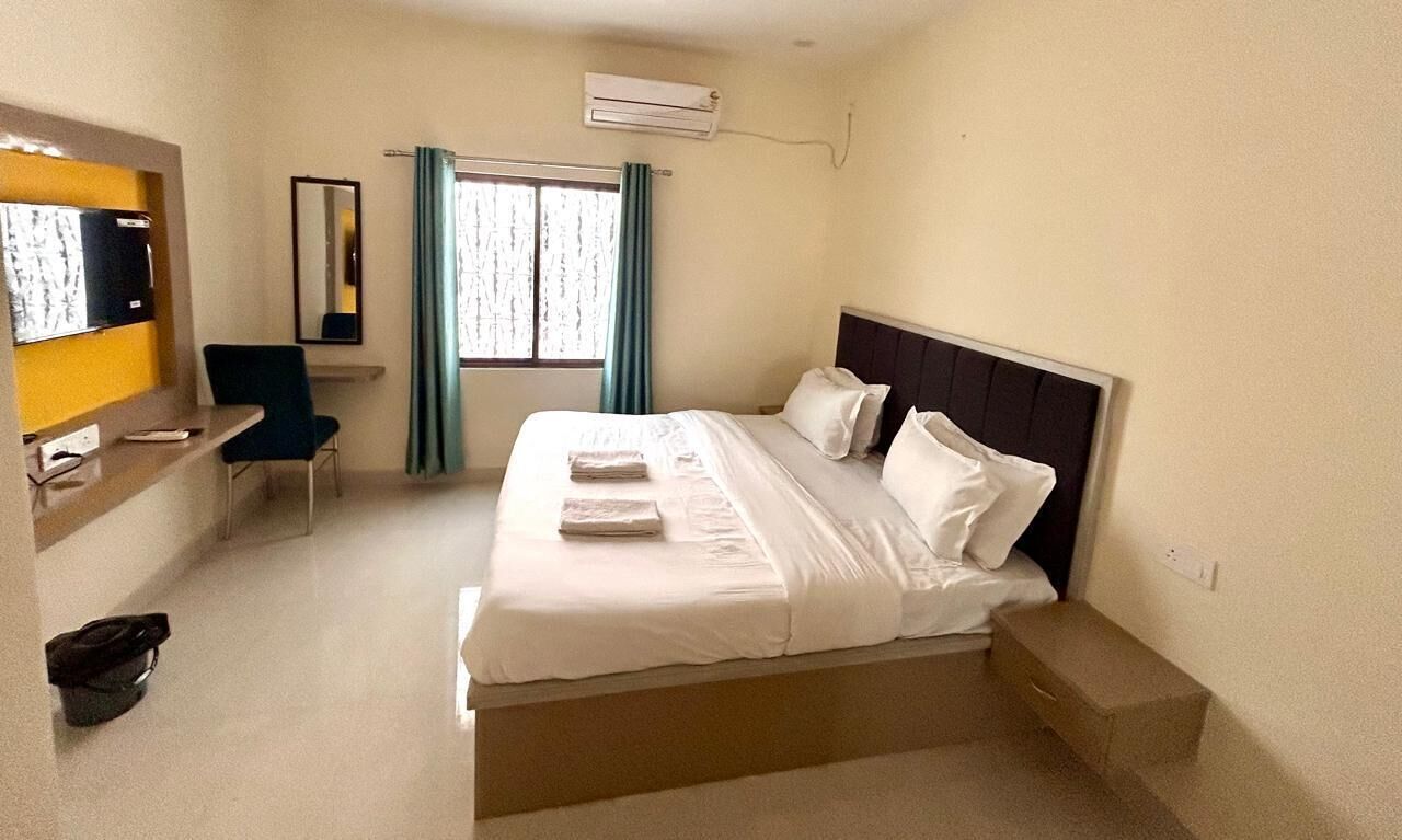 A hotel room with a bed, a desk with a chair, a mirror, and a window with curtains.