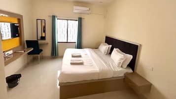 A hotel room with a bed, a desk with a chair, a mirror, and a window with curtains.
