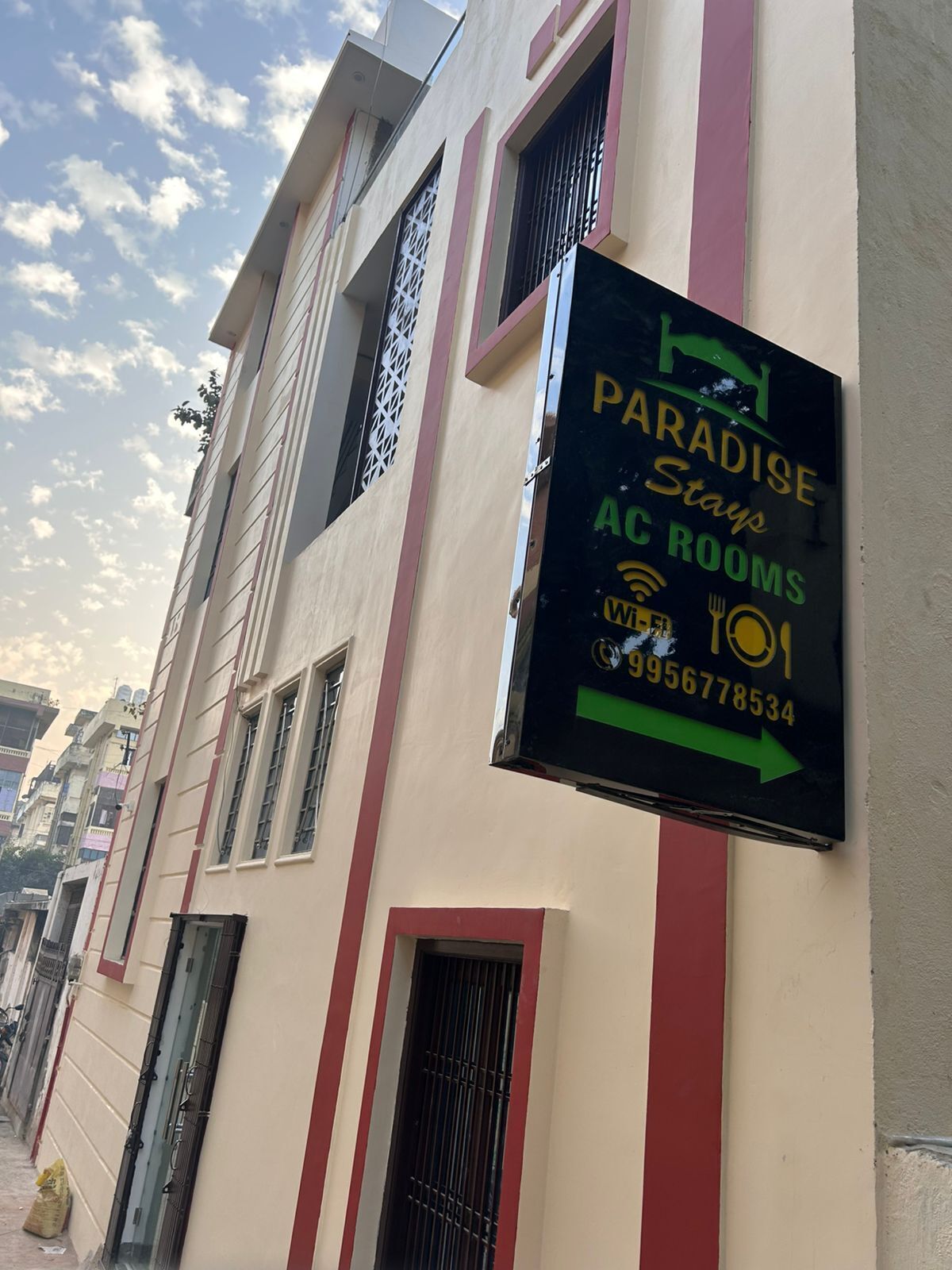 Un edificio con un letrero que anuncia "Paradise Stay AC Rooms" y un número de contacto.