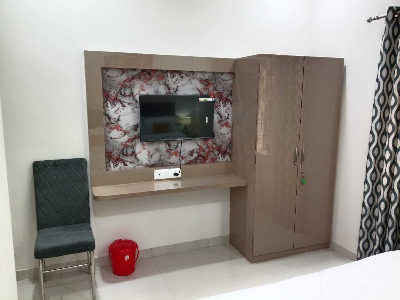 A room with a TV mounted on a marble wall, a wardrobe, a chair, and a red bucket.