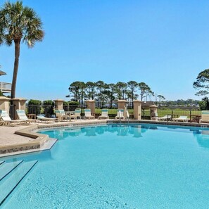 A clear blue swimming pool with lounge chairs and a palm tree, surrounded by a fence and greenery. - Charming 2-bedroom condo in desirable Sandestin Resort, GOLF CART INCLUDED!! (Destin)