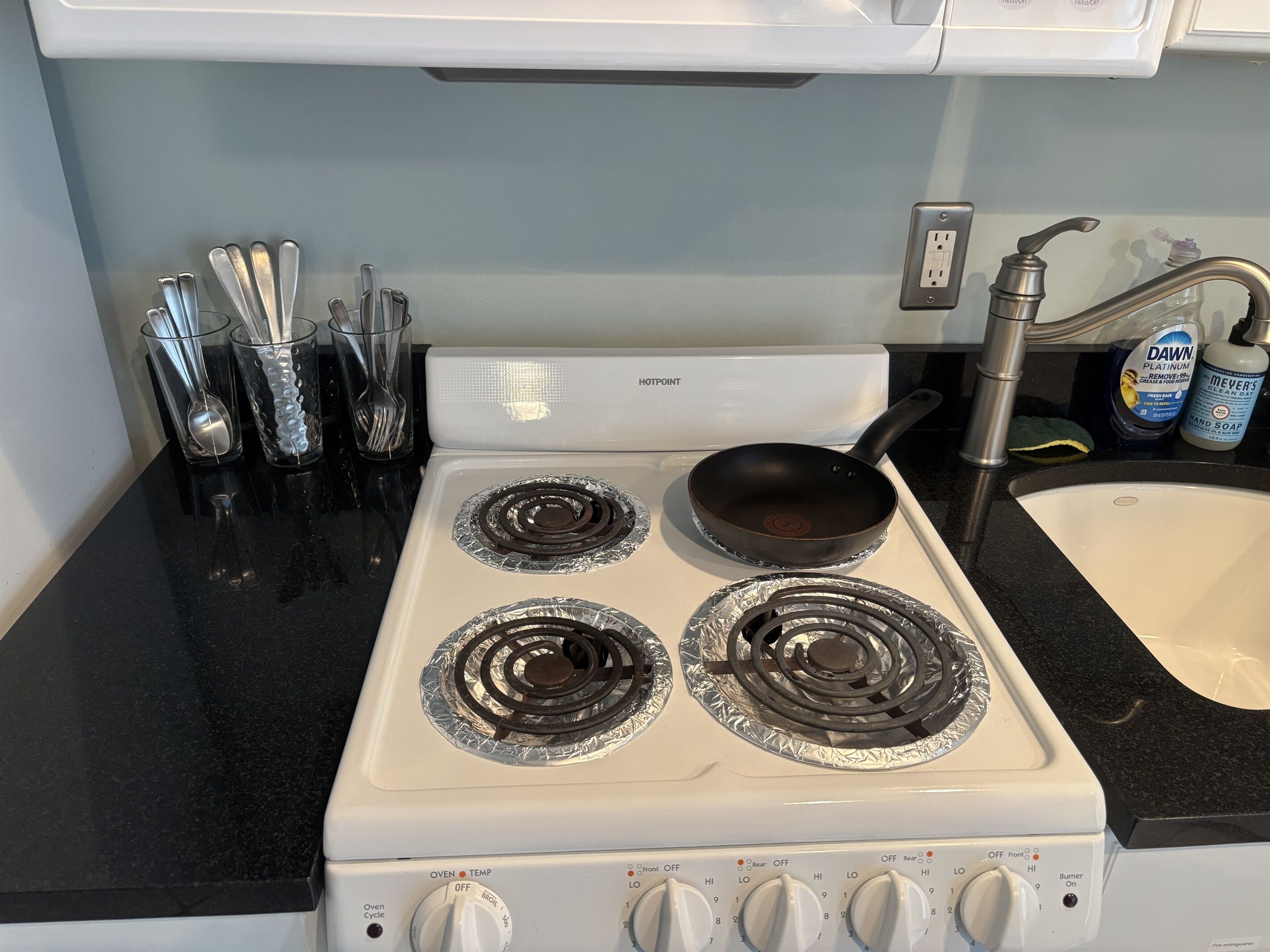 Een keuken met een witte kookplaat, twee branders, en een zwarte koekenpan op de linker brander.