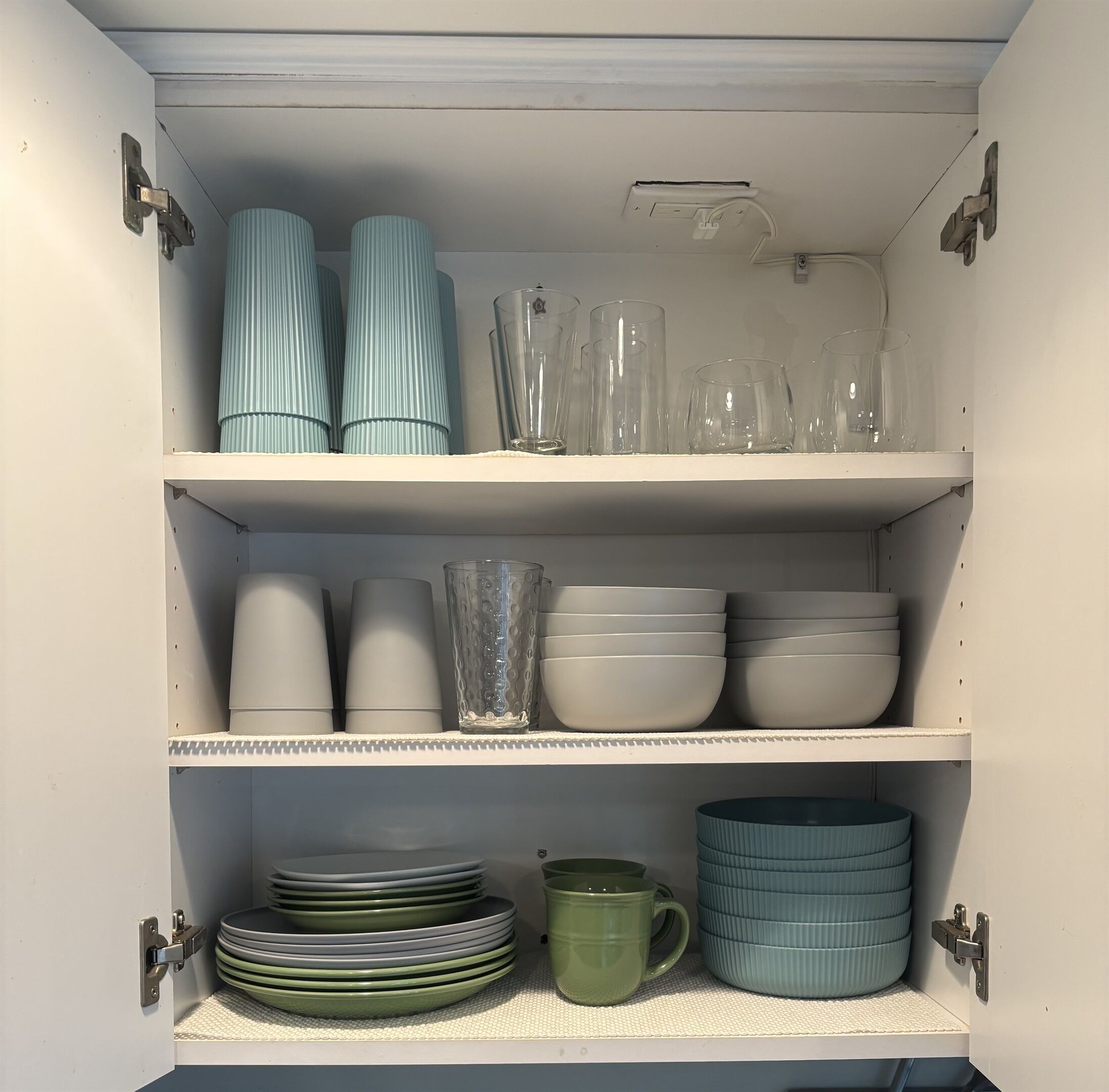 Un armario de cocina con estantes que contienen diferentes vasos, cuencos y platos.