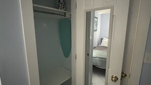 Ein schmaler Flur mit einer weißen Tür, die zu einem Schlafzimmer führt. Ein grünes Handtuch hängt an der Wand, und ein kleines Regal mit einem dekorativen Gegenstand ist sichtbar.