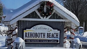 Ein hölzernes Schild mit der Aufschrift 'Welcome to Rehoboth Beach' und 'The Nation's Summer Capital', umgeben von Schnee und Weihnachtsdekorationen.