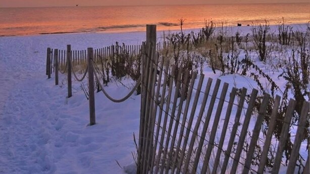 Ein verschneiter Strand mit einer Holzlattenveranda und einem Sonnenuntergang.