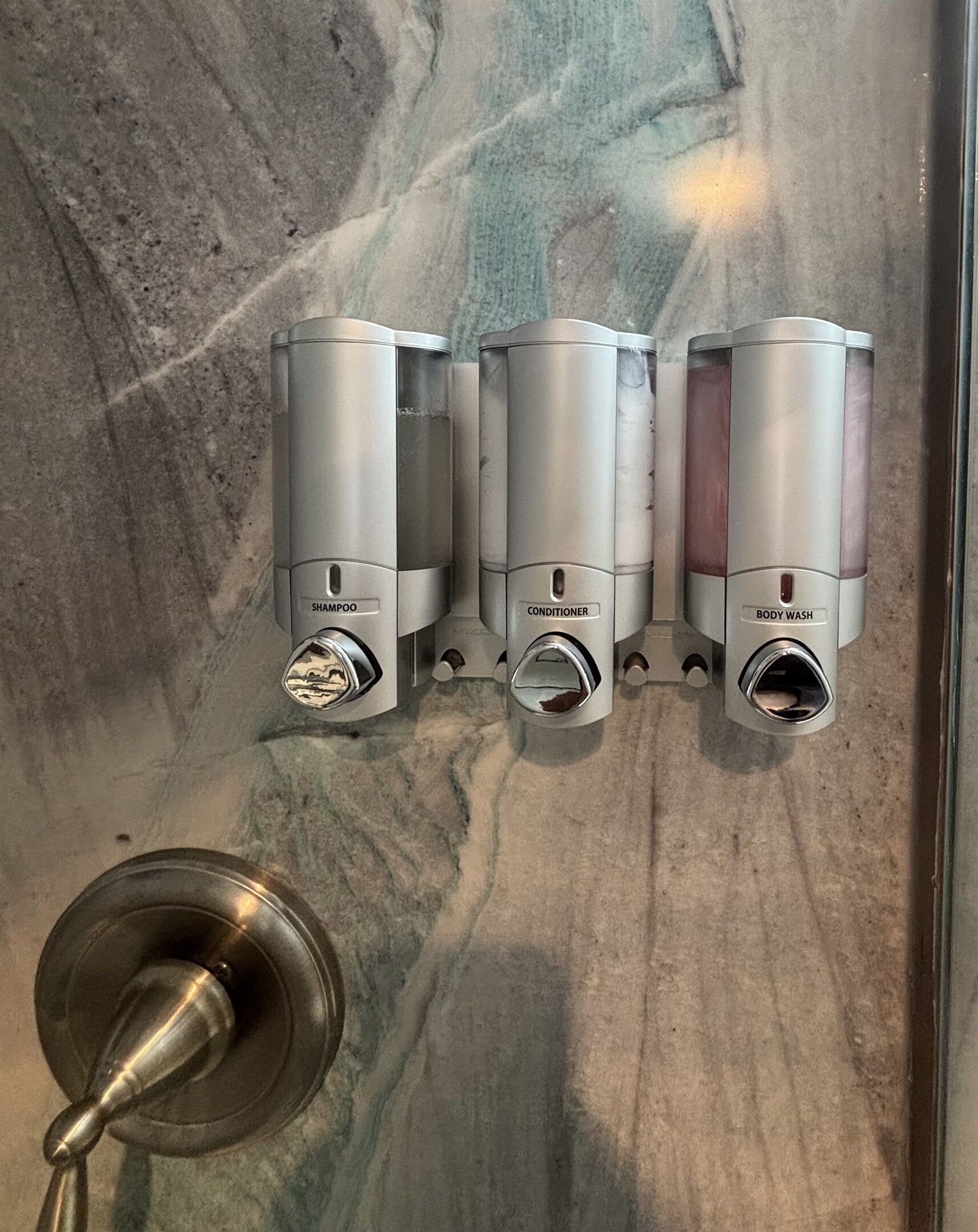 A bathroom with three wall-mounted dispensers labeled "shampoo," "conditioner," and "body wash."