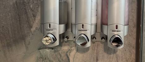 A bathroom with three wall-mounted dispensers labeled "shampoo," "conditioner," and "body wash."