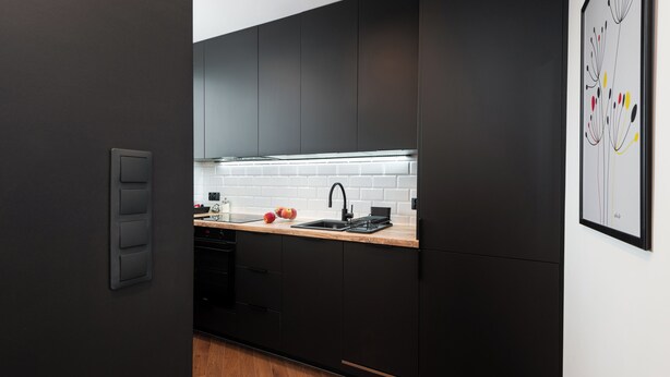A modern kitchen with dark cabinetry, a white brick backsplash, and a wooden countertop. - Crystal - by Kairos Apartments (Gliwice)
