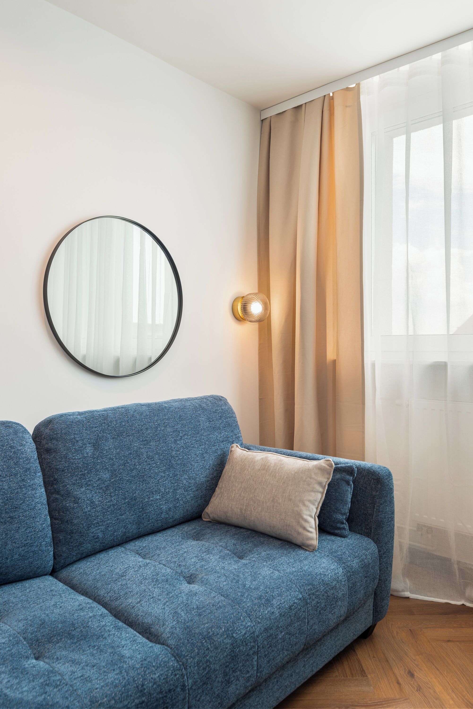 Ein blaues Sofa, ein runder Spiegel und eine Lampe an der Wand.