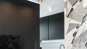 A modern kitchen with dark cabinetry, a wooden herringbone floor, and a black and white abstract wall art piece. - Crystal - by Kairos Apartments (Gliwice)