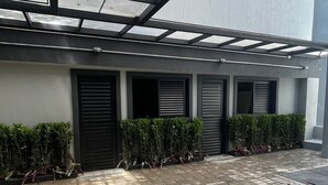 A covered outdoor area with a paved walkway, potted plants, and closed shutters on the building facade. - ADD HOTÉIS Congonhas (Sao Paulo)