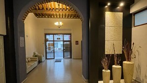 A hotel lobby with a tiled floor, a sofa, a chandelier, and three large vases with plants. - Hotel Santa Julia  (Tecamachalco)