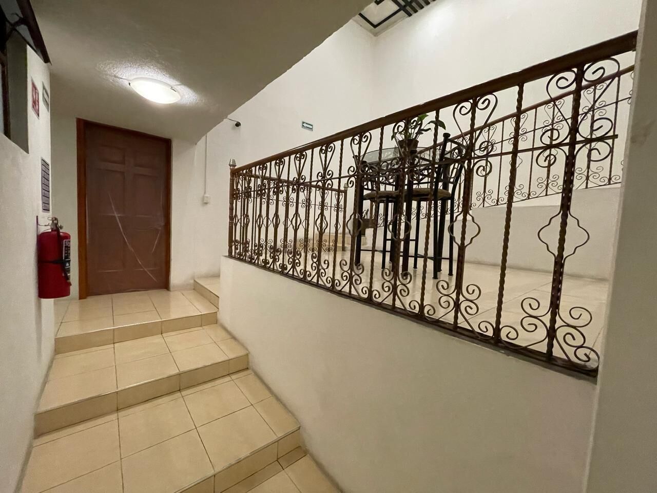 A staircase with beige tiles, a metal railing with decorative patterns, and a red fire extinguisher on the wall.