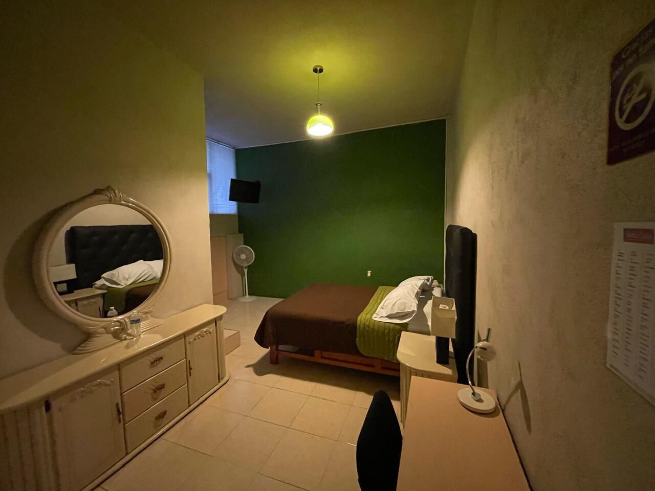 Un dormitorio con cama, mesita de noche, espejo, cómoda y pared verde.