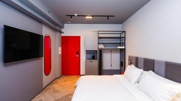 Una habitación de hotel moderna con una cama grande, un televisor de pantalla plana montado en la pared, una puerta roja y un armario empotrado con estantes.