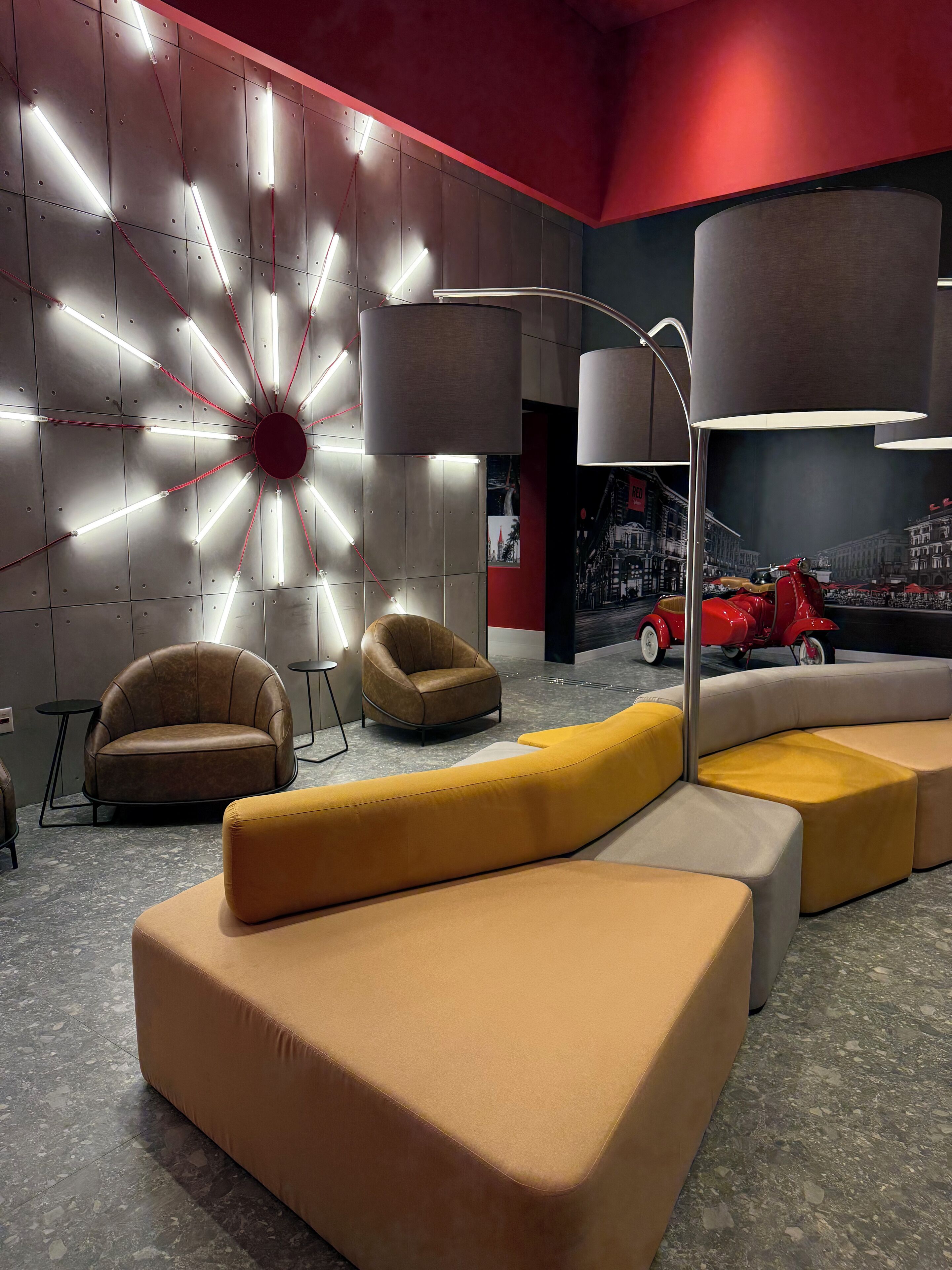 A modern lounge area with a geometric light installation, leather armchairs, and a mural of a cityscape.