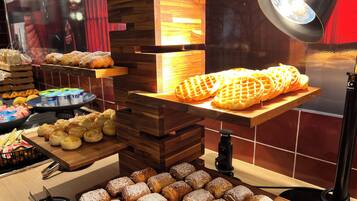 Una vitrina de pastelería con diversos pasteles y pan, incluyendo gofres y croissants, dispuestos sobre soportes de madera y una tabla de madera.