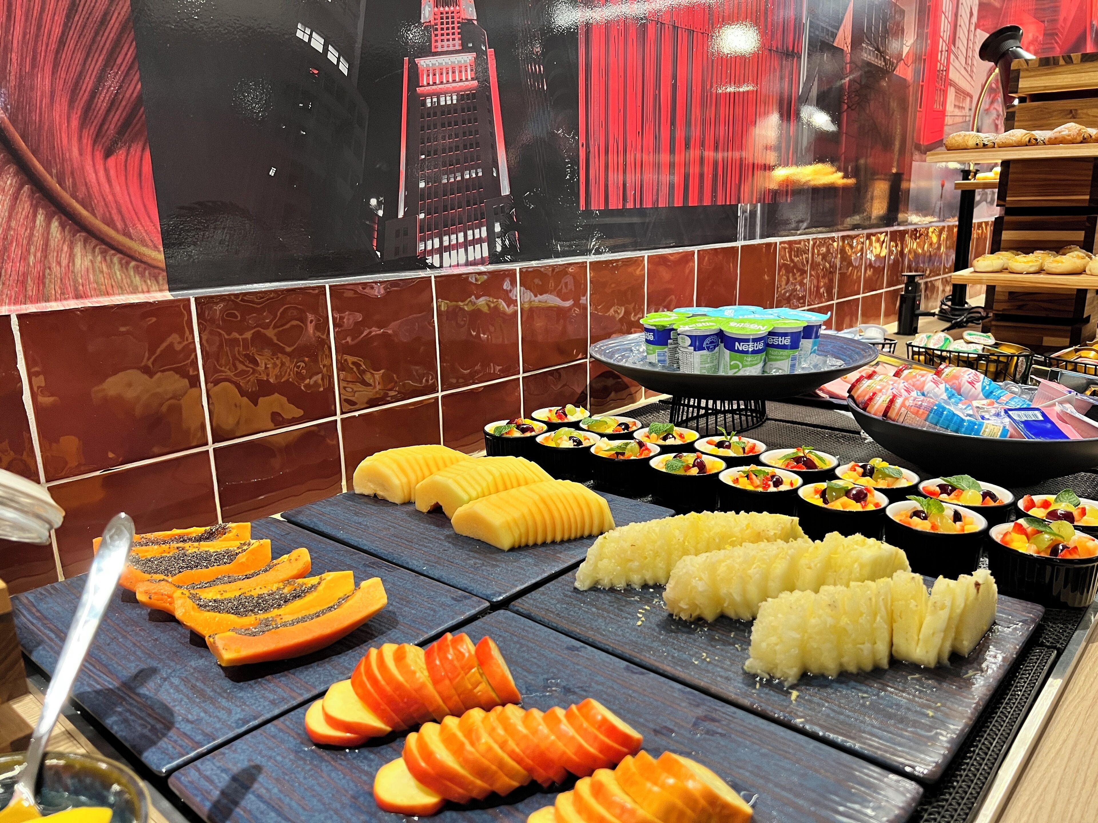 Buffet com diversos alimentos, incluindo frutas fatiadas e produtos embalados.