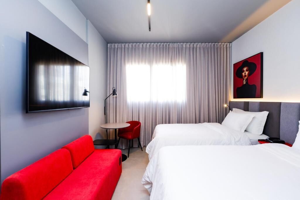 A hotel room with two beds, a red sofa, a small table, and a TV mounted on the wall.