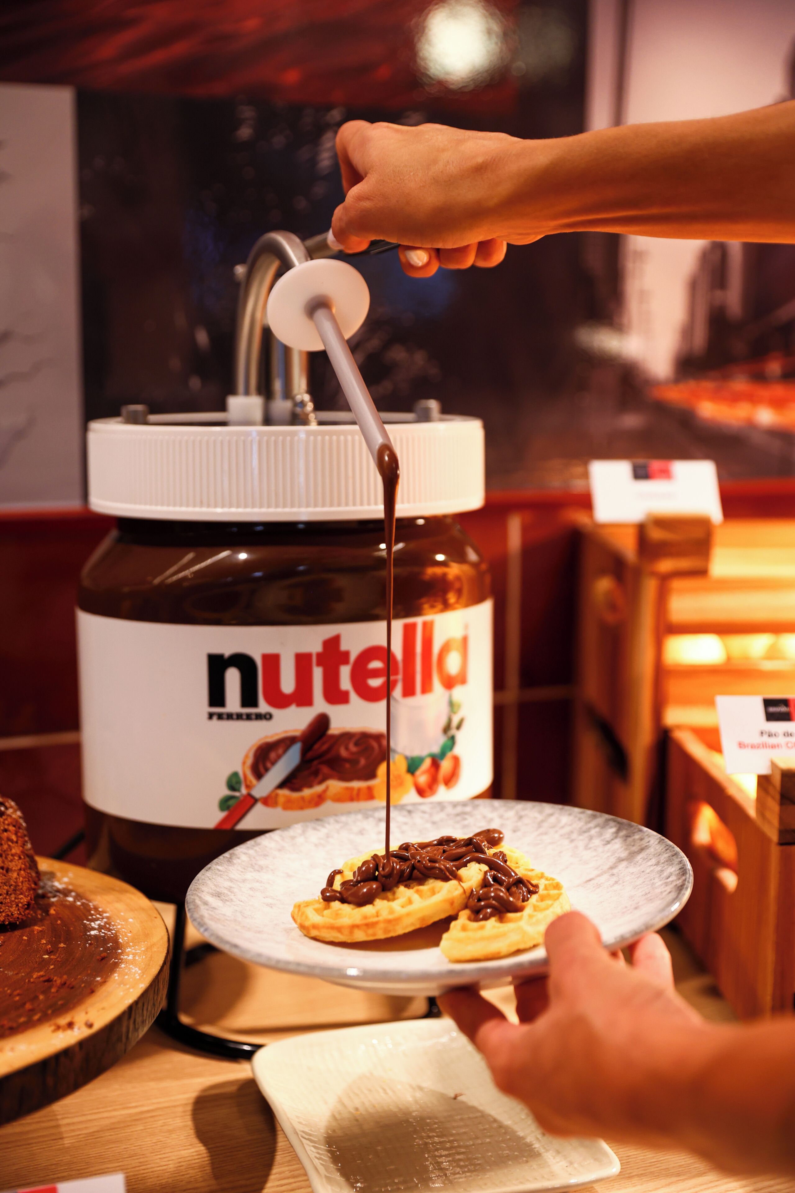 A hand pouring Nutella from a jar onto a plate with a waffle.