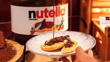 A hand pouring Nutella from a jar onto a plate with a waffle.