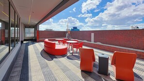 A rooftop terrace with red seating, a tiled floor, and a view of the sky and clouds. - Radisson RED Ibirapuera (Sao Paulo)