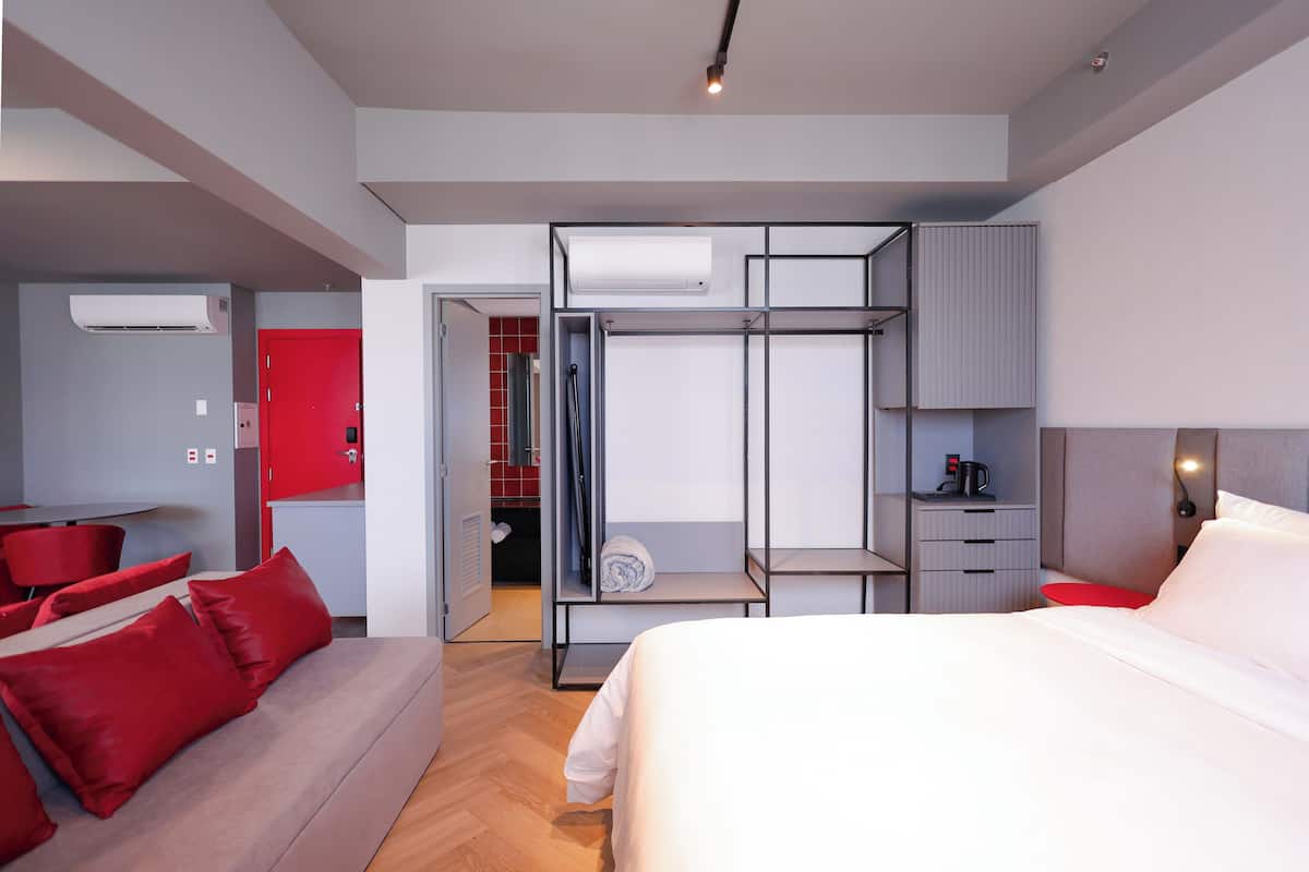 A modern hotel room with a bed, a red sofa, a desk, and a wardrobe.